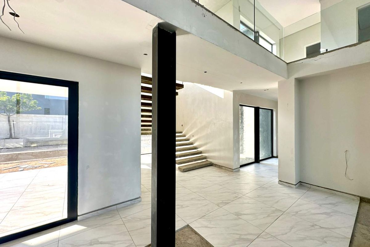 Spacious open-plan living area under construction, featuring a modern staircase, mezzanine level with glass balustrade, and large sliding doors leading to the exterior.