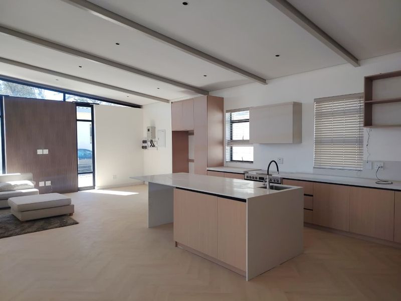Modern open-plan kitchen and living area featuring light wood cabinetry, a central island with stone countertops, and elegant herringbone flooring.