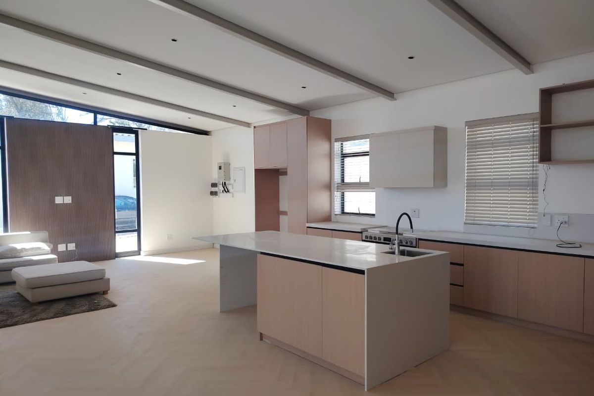 Modern open-plan kitchen and living area featuring light wood cabinetry, a central island with stone countertops, and elegant herringbone flooring.