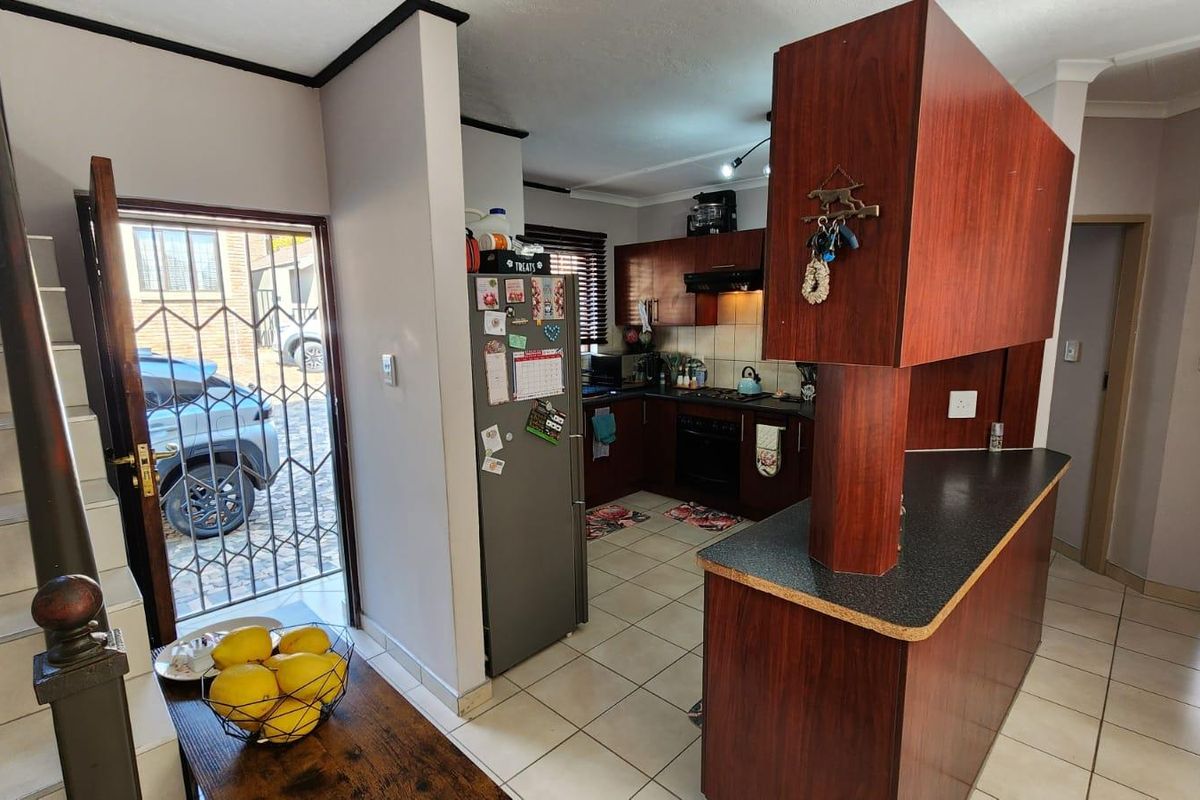 A functional kitchen featuring dark wood cabinetry, laminate countertops, and tiled flooring, with an open-plan layout adjacent to the entrance and staircase.