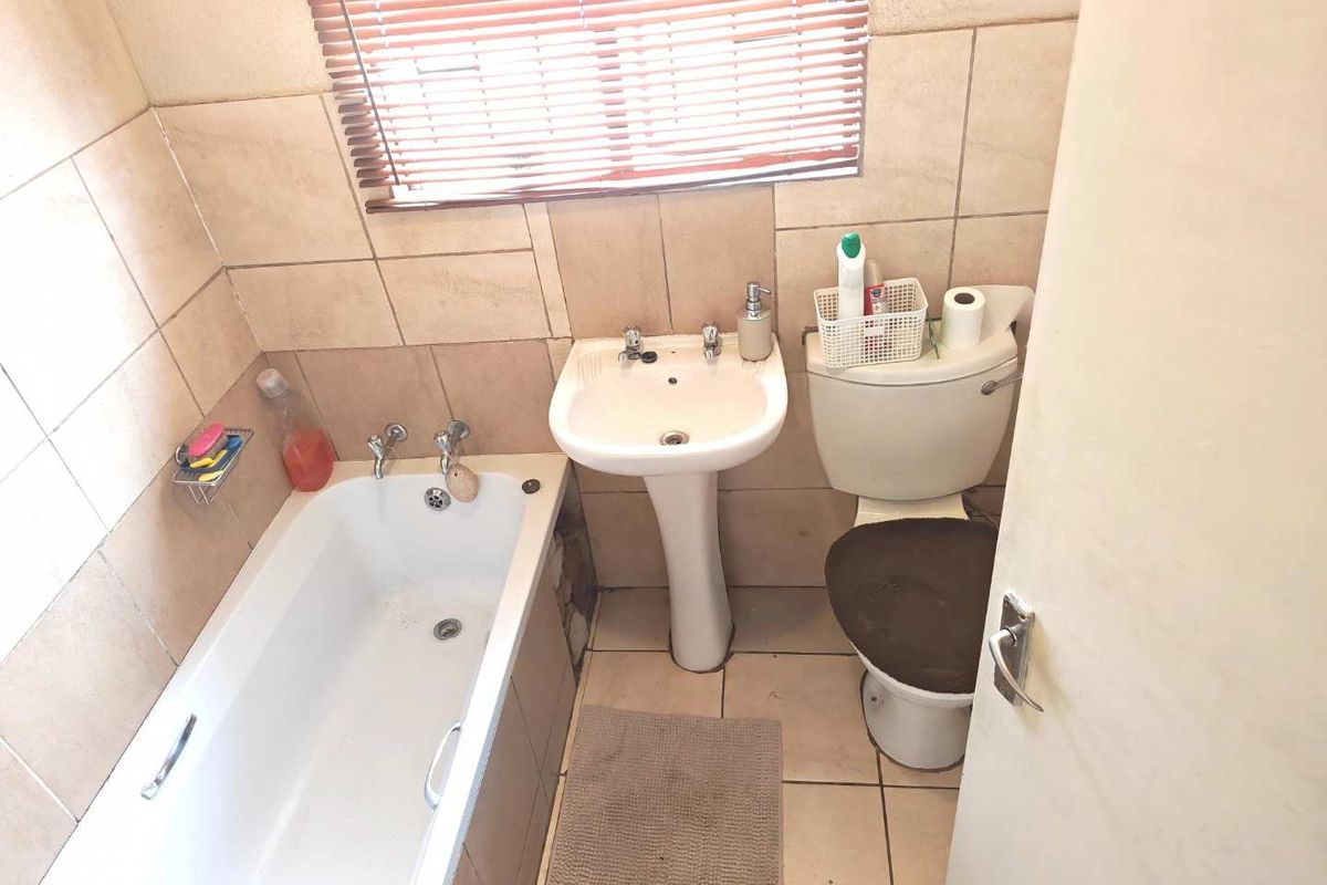 A compact bathroom featuring a pedestal basin, bathtub, and toilet with neutral wall and floor tiling.