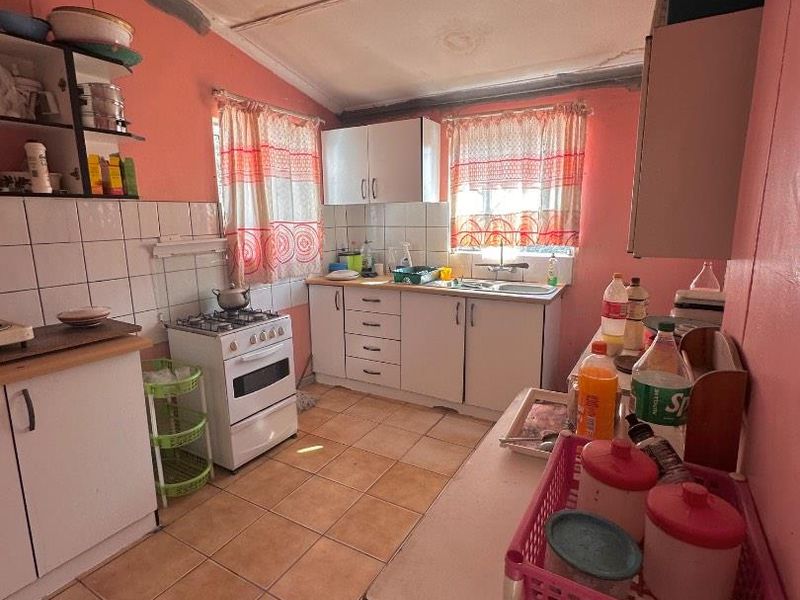 A dated kitchen featuring tiled flooring, a tiled backsplash, built-in cabinetry, and a freestanding stove, requiring cosmetic updates to modernize the space.