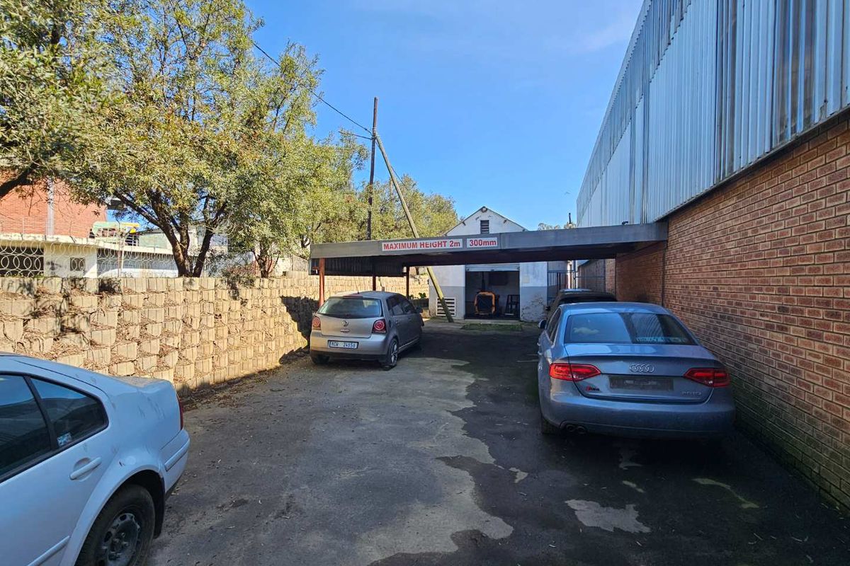 Rear exterior area featuring a concrete block boundary wall, asphalt driveway, and a metal carport structure attached to the industrial building.