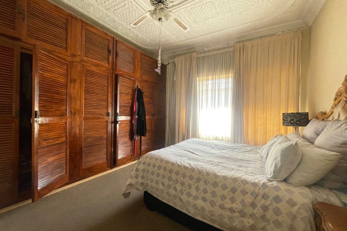 A bedroom featuring extensive built-in wooden cabinetry, a classic ornate pressed metal ceiling, and a ceiling fan.