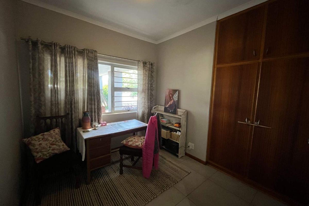 A bedroom featuring built-in wooden cupboards, tiled flooring, and a window with curtaining.