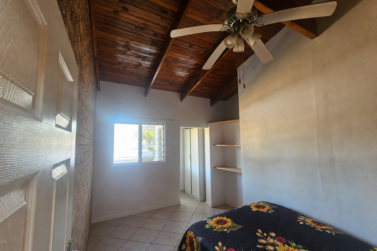 Bedroom featuring a vaulted timber-paneled ceiling, exposed brick feature wall, tiled flooring, built-in shelving, and a ceiling fan.