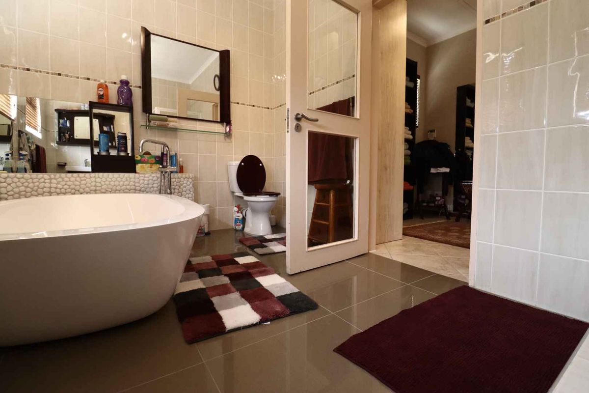 A bathroom featuring a freestanding bathtub, tiled walls and flooring, and a toilet, with an adjacent doorway leading to a dressing area.