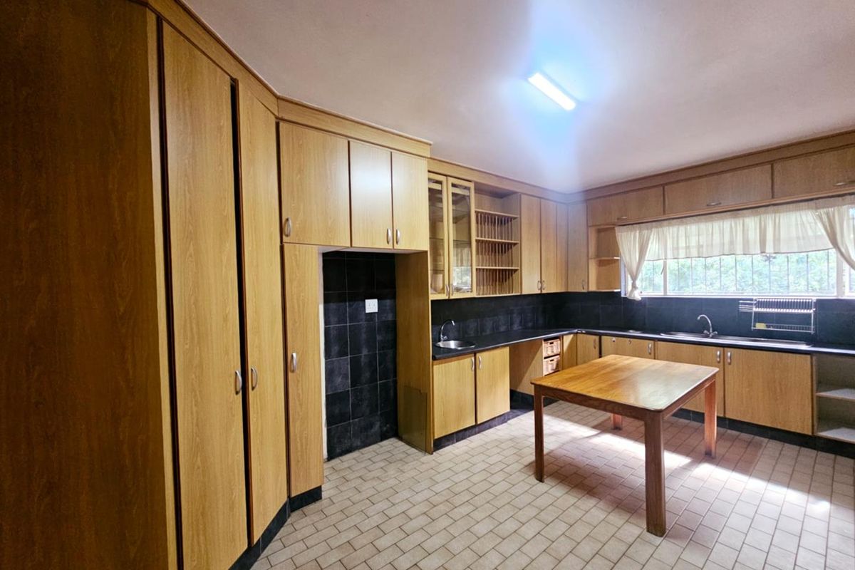 A spacious kitchen featuring extensive wood-finish cabinetry, dark countertops, tiled flooring, and a central island, offering a functional layout with ample storage.
