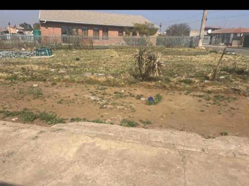 A vacant residential plot featuring a concrete driveway and perimeter fencing, offering a clear space for potential development.