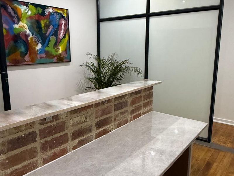 Modern office space featuring a custom exposed brick reception counter with stone top and a sleek black-framed glass partition.