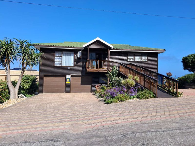 Front elevation of a timber-clad house featuring a double garage, paved driveway, and a raised timber deck with an external staircase.