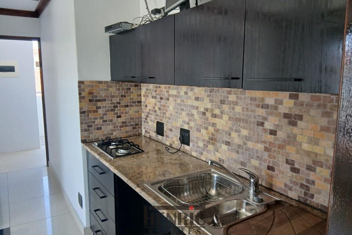 Compact kitchen featuring dark cabinetry, granite countertops, a built-in gas hob, and a stainless steel sink with a mosaic tile backsplash.