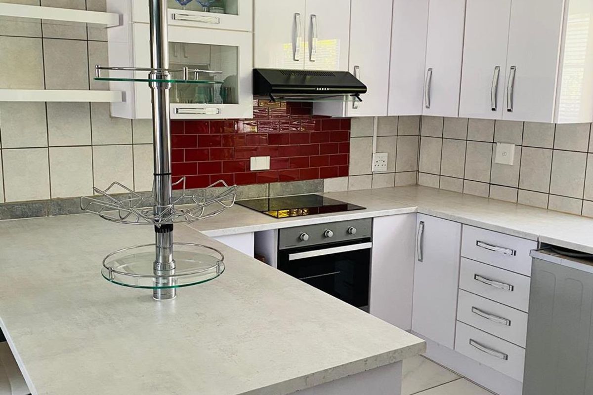 A functional kitchen featuring white cabinetry, contrasting red tiled backsplash, built-in oven, electric hob, and a breakfast bar with stone-look countertops.