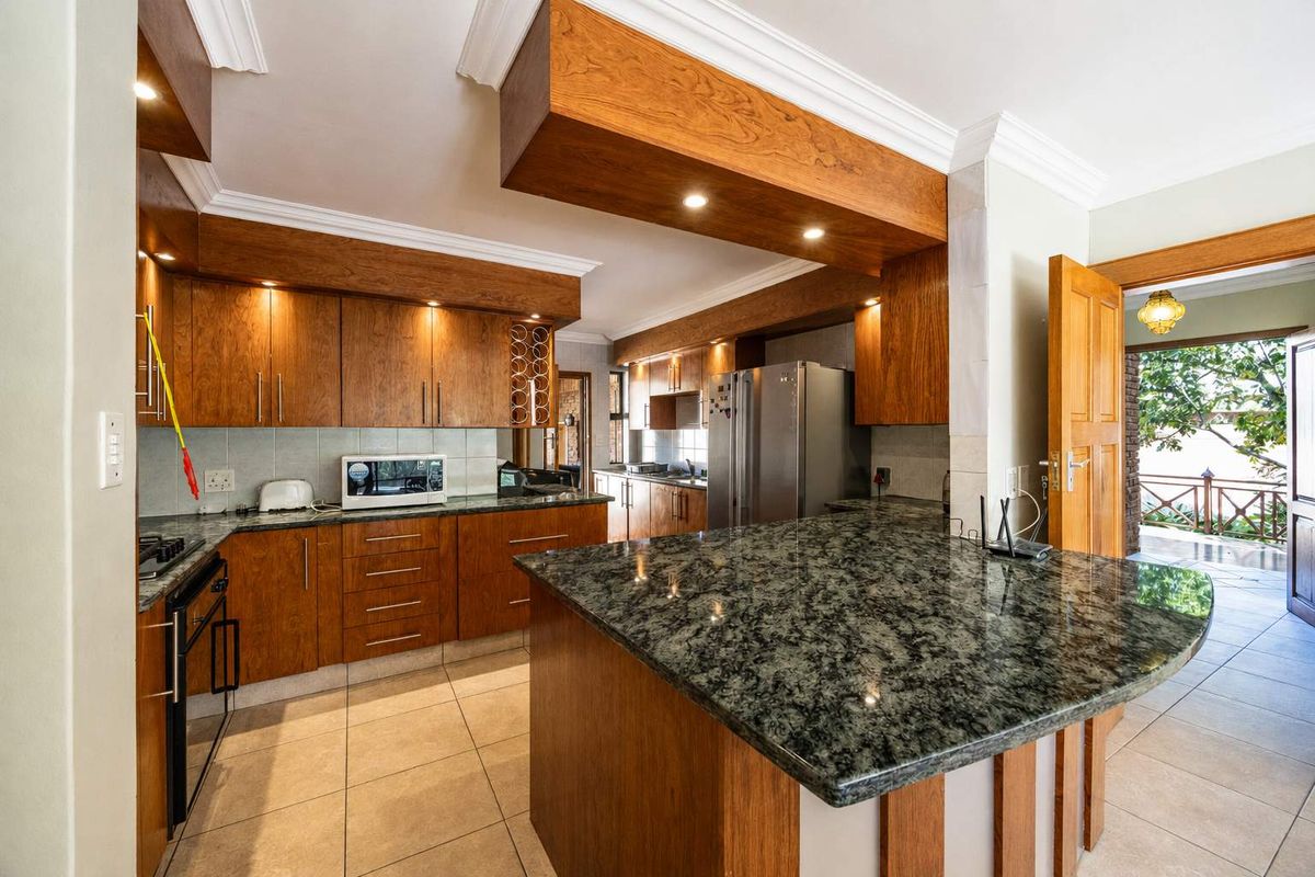 Spacious kitchen featuring warm wooden cabinetry, granite countertops, a central island, and integrated appliances, with direct access to an outdoor patio area.
