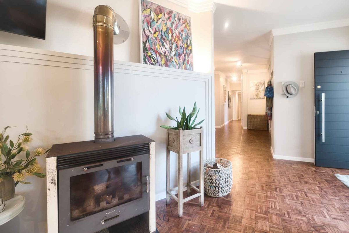 A welcoming living area featuring a prominent freestanding fireplace, classic parquet flooring, and a direct view into the home's hallway.
