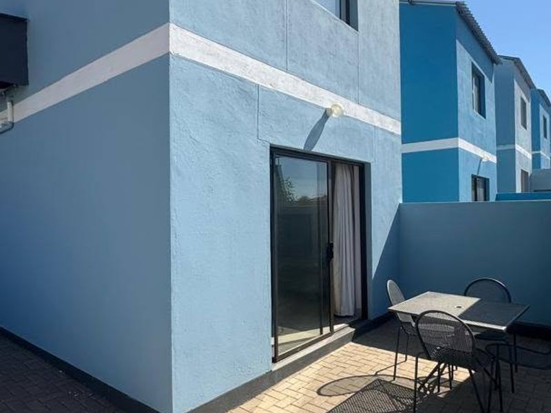 Rear exterior view of the townhouse featuring a paved patio area and a sliding glass door providing access to the interior.