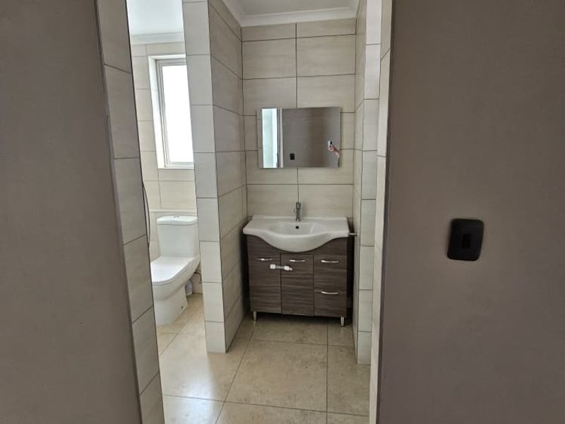 A clean, modern bathroom featuring a vanity cabinet with a ceramic basin, a wall-mounted mirror, and a separate toilet area with neutral tiling.