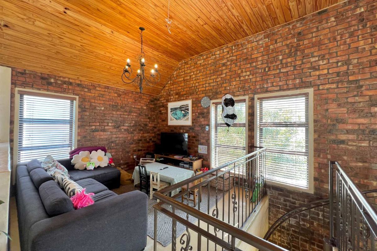 A characterful living area featuring exposed brick walls, a high timber-clad vaulted ceiling, and a wrought iron balustrade overlooking a spiral staircase.