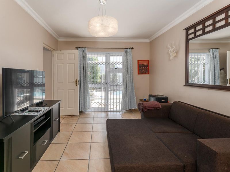 A living room featuring tiled flooring, cove cornicing, and a security gate leading to an outdoor area.
