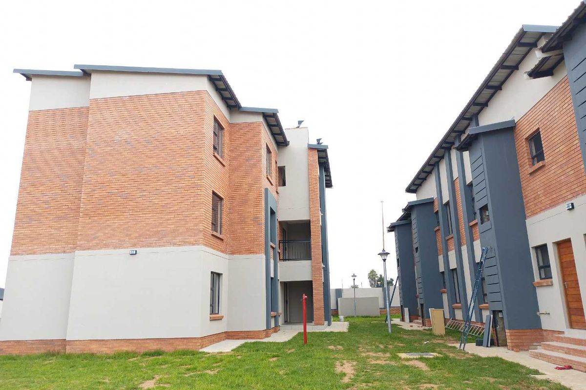 Exterior view of a modern apartment complex featuring face brick and plastered facades with paved walkways and communal garden space.