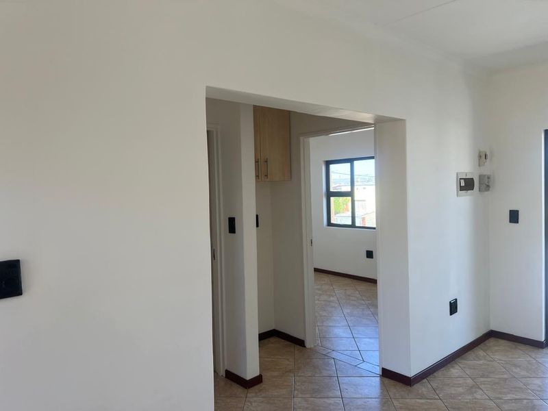 A clean, neutral hallway featuring tiled flooring and built-in cabinetry, providing a bright and functional transition space between rooms.