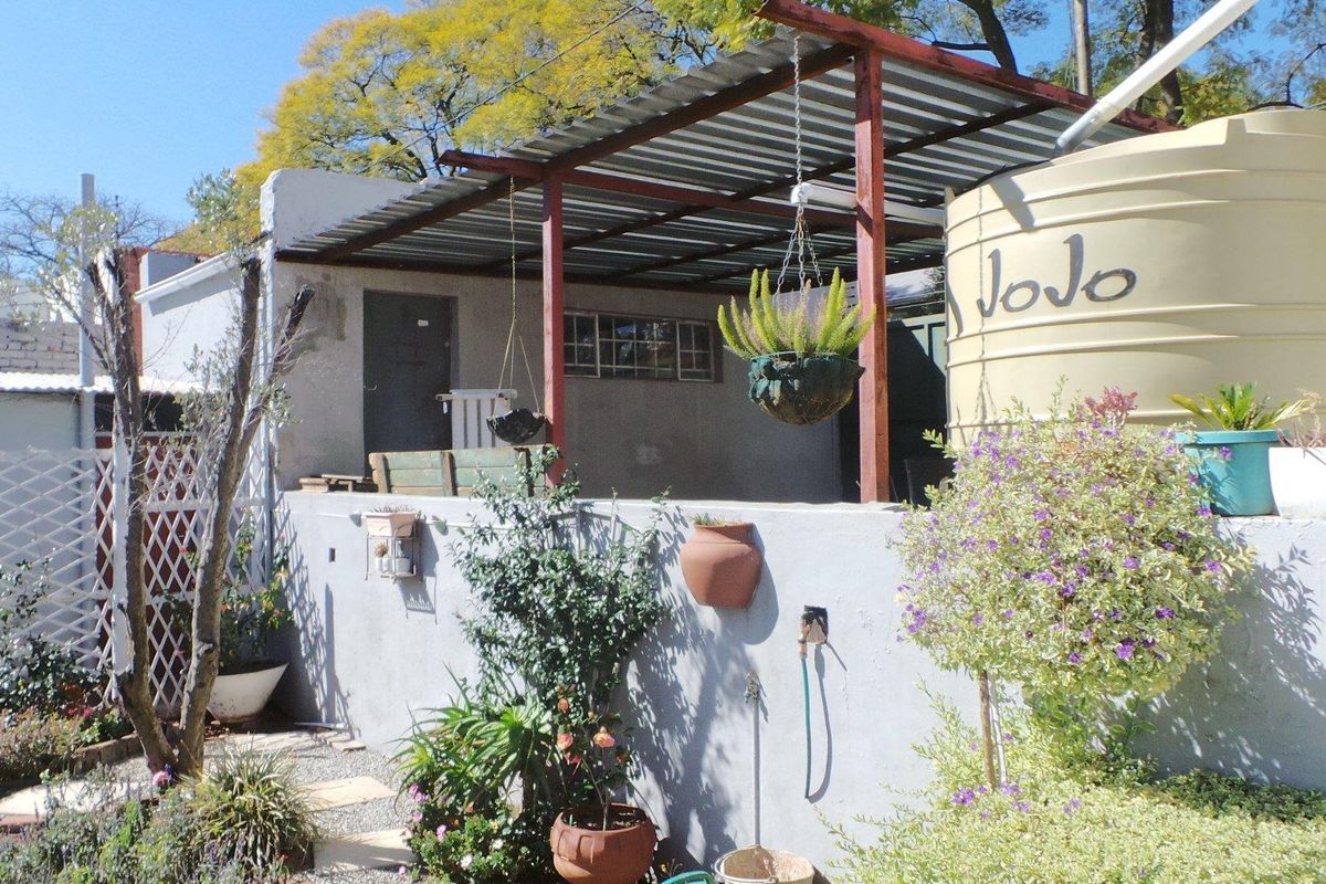 Rear exterior area featuring a covered patio structure, masonry wall, and a large water storage tank in a garden setting.