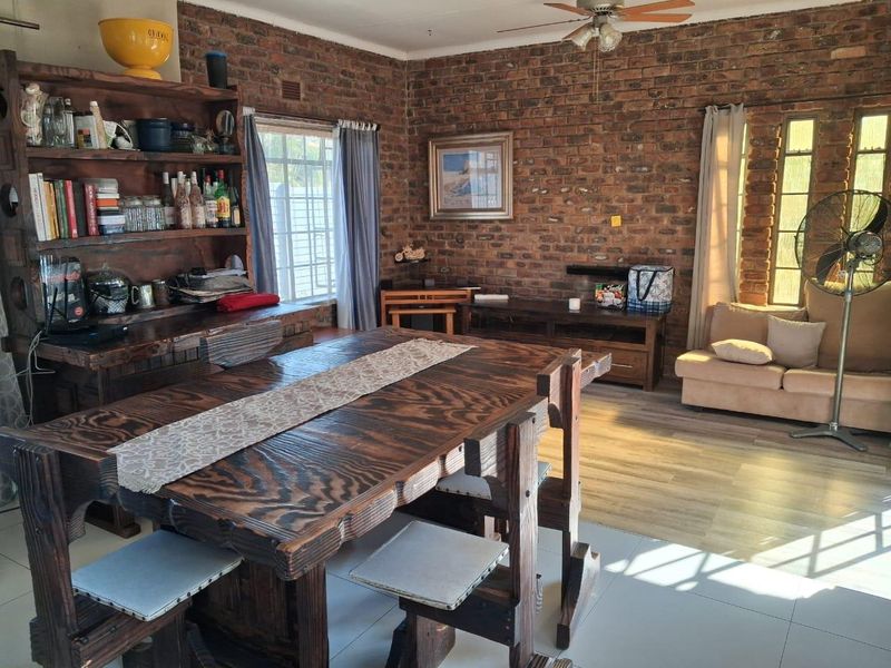 A living area featuring exposed brick walls, a ceiling fan, and a combination of tiled and laminate flooring.