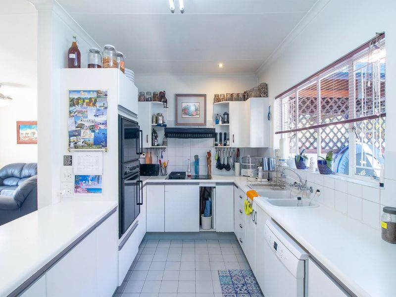 A functional kitchen featuring white cabinetry, built-in oven, cooktop, and tiled splashback, with a view into the adjacent living area.