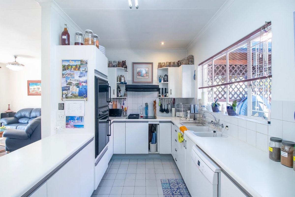 A functional kitchen featuring white cabinetry, built-in oven, cooktop, and tiled splashback, with a view into the adjacent living area.