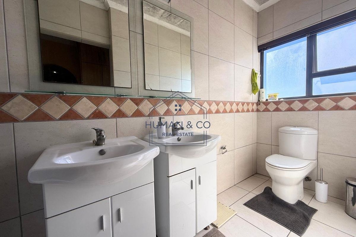 A functional bathroom featuring dual vanity basins with storage cabinets, a standard toilet, and tiled walls with a decorative border.