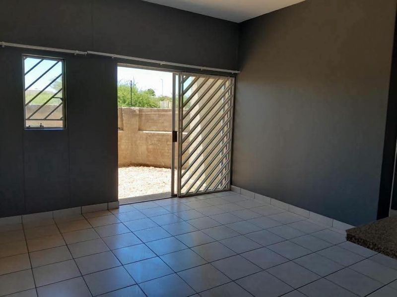 An empty living area featuring tiled flooring and a sliding glass door with a security gate leading to an outdoor space.
