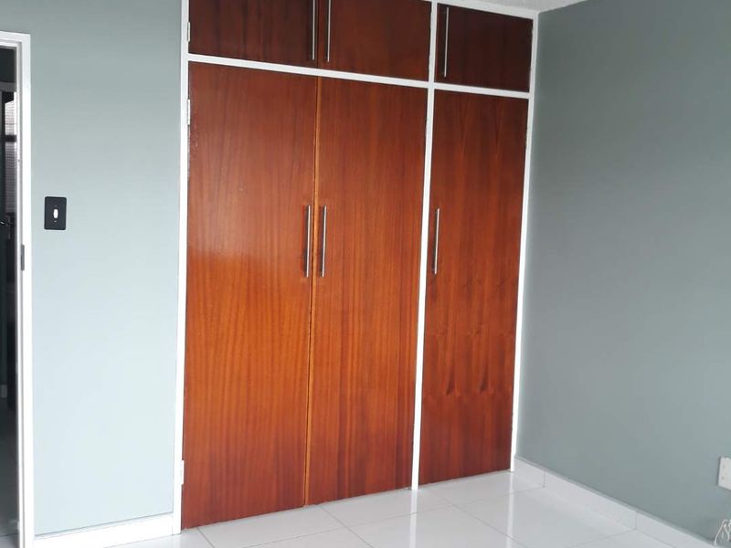 A clean, empty bedroom featuring polished white floor tiles and floor-to-ceiling wooden built-in cupboards with overhead storage compartments.