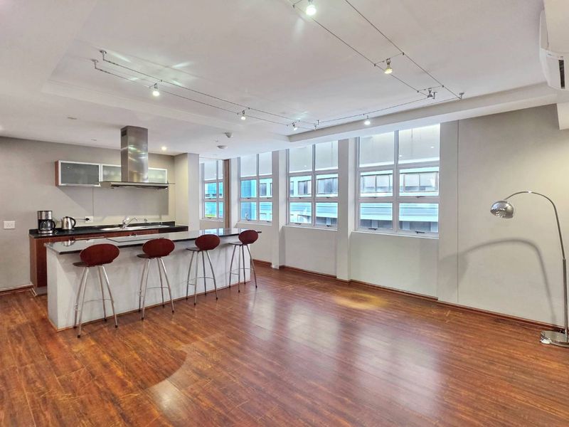Spacious open-plan living area featuring a modern kitchen with granite island, track lighting, and large windows providing ample natural light.