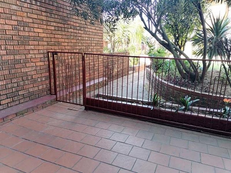 A paved outdoor patio area featuring a brick wall, metal security gate, and a landscaped garden path with a retaining wall.