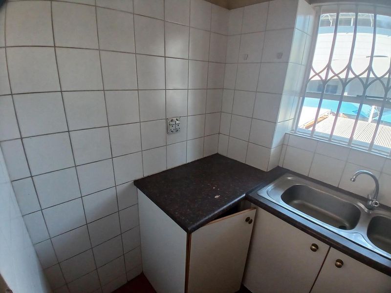 A compact kitchen area featuring tiled walls, a stainless steel sink, and built-in cabinetry with a laminate countertop.