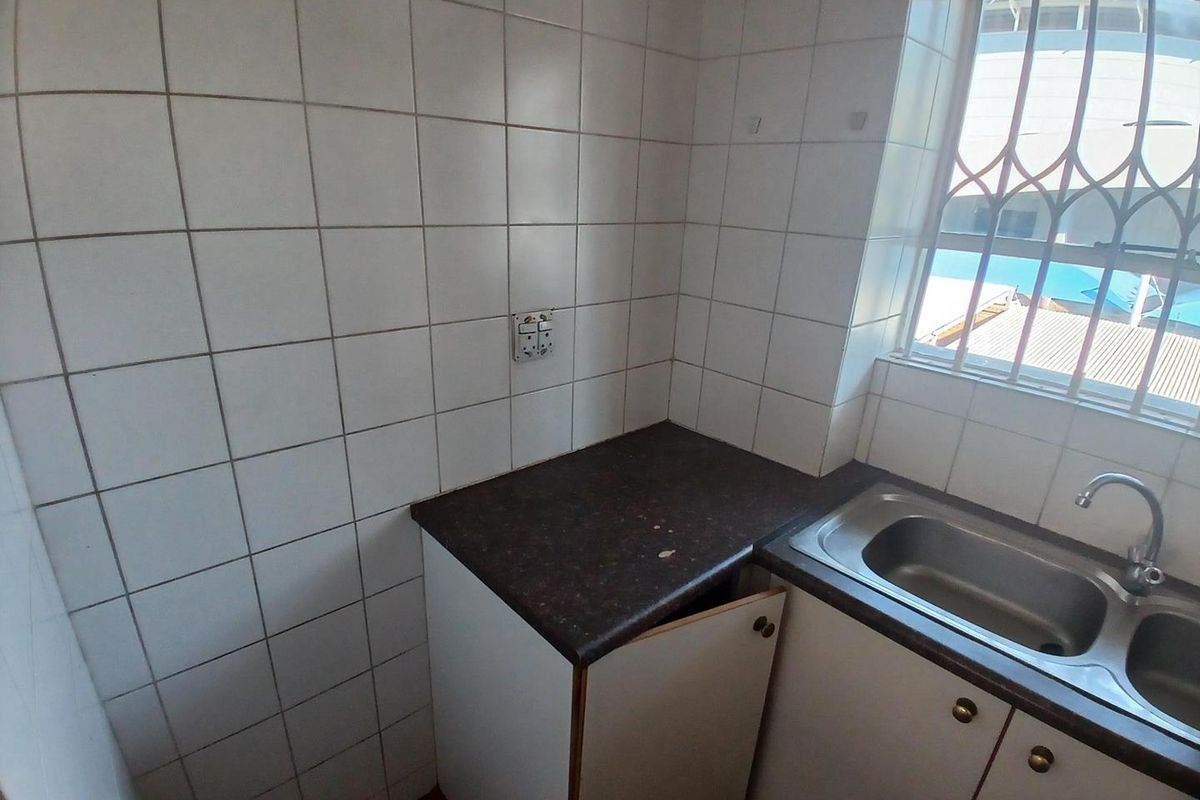 A compact kitchen area featuring tiled walls, a stainless steel sink, and built-in cabinetry with a laminate countertop.