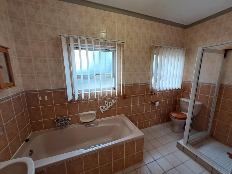 A functional bathroom featuring a built-in bathtub, separate shower enclosure, and toilet, finished with neutral wall and floor tiling.