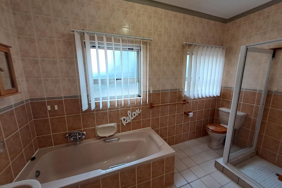 A functional bathroom featuring a built-in bathtub, separate shower enclosure, and toilet, finished with neutral wall and floor tiling.