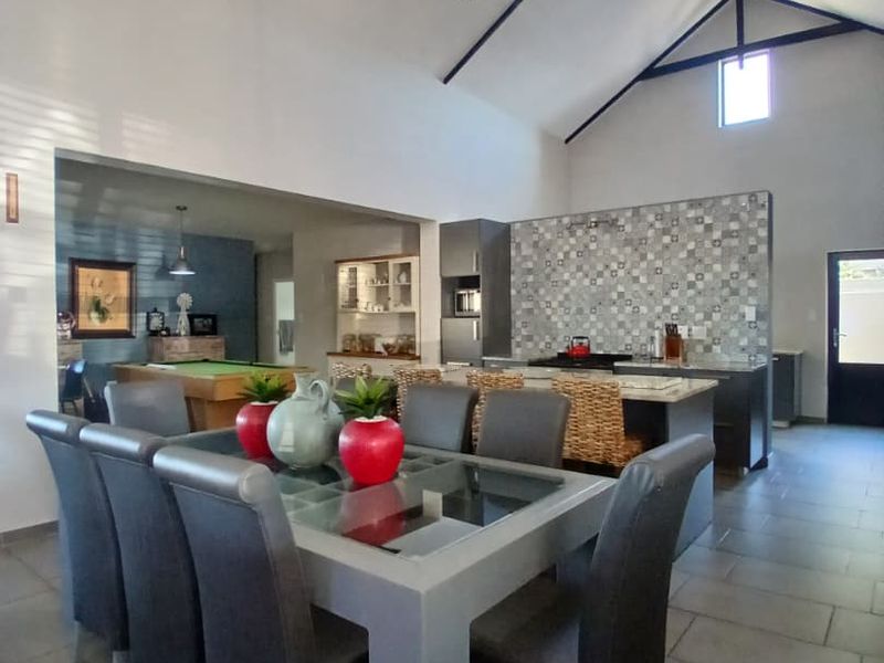 Spacious open-plan living and dining area featuring a high vaulted ceiling with exposed trusses, a modern kitchen island, and contemporary tiled finishes.