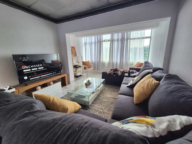 A comfortable living room featuring tiled flooring, large windows allowing natural light, and a unique decorative ceiling finish.