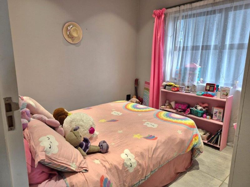 A standard bedroom featuring tiled flooring and a window with curtain treatments, currently utilized as a child's bedroom.