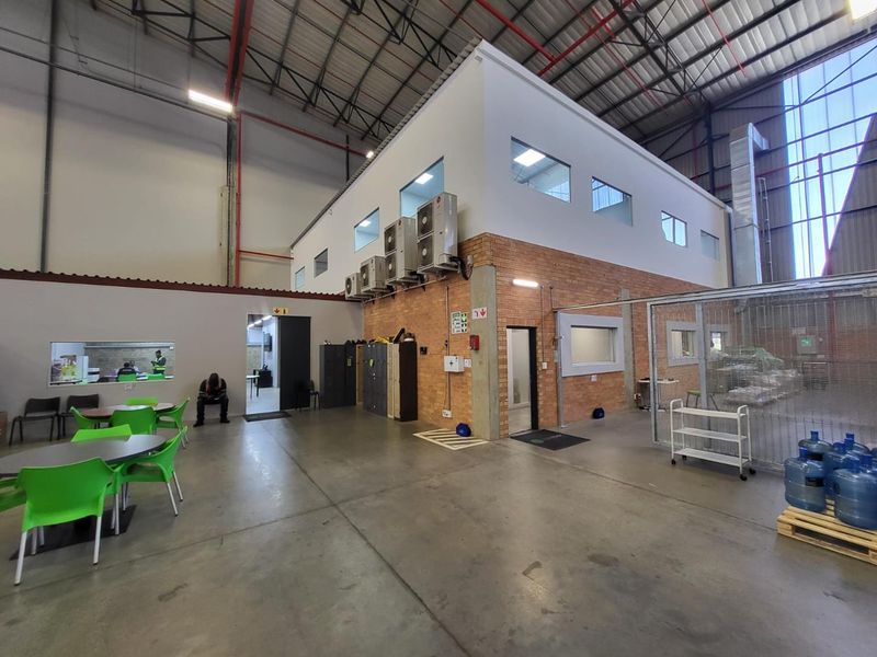 Spacious industrial warehouse interior featuring a multi-level office block, exposed steel roof trusses, concrete flooring, and integrated wall-mounted air conditioning units.