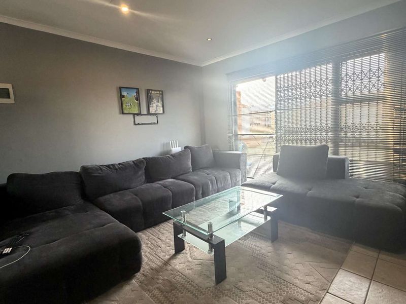 A living room featuring tiled flooring, recessed downlights, and a large window fitted with security gates and venetian blinds.