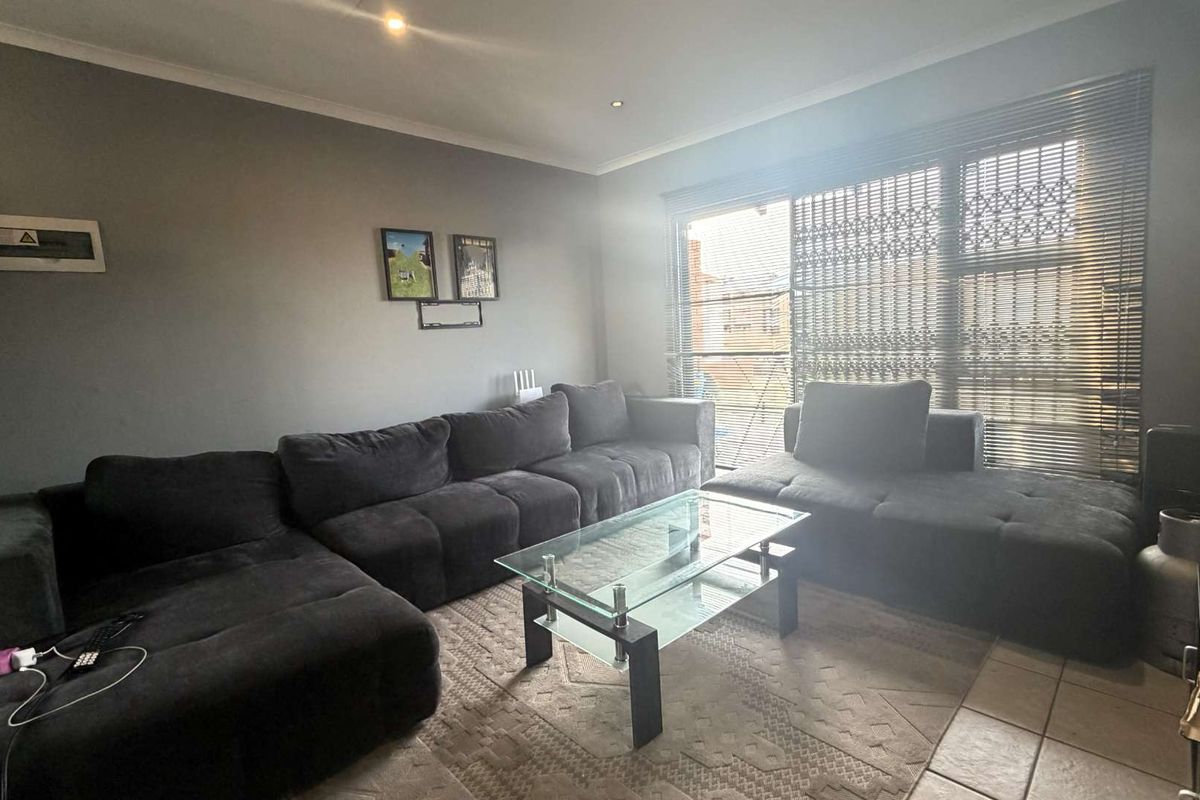A living room featuring tiled flooring, recessed downlights, and a large window fitted with security gates and venetian blinds.