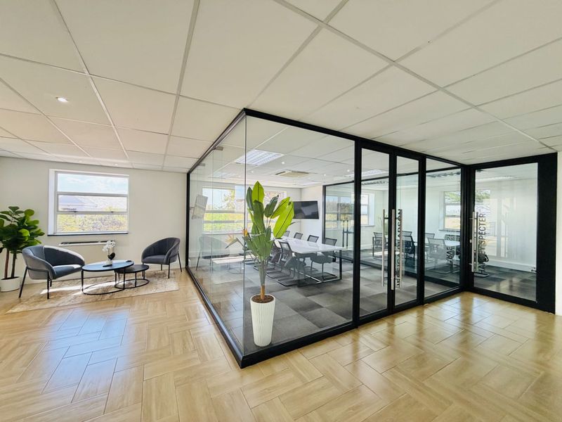 Modern office space featuring a glass-enclosed meeting room, herringbone flooring, and a professional open-plan reception area with excellent natural light.