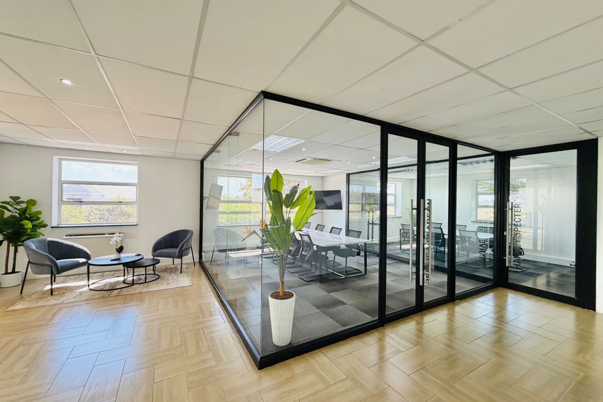Modern office space featuring a glass-enclosed meeting room, herringbone flooring, and a professional open-plan reception area with excellent natural light.