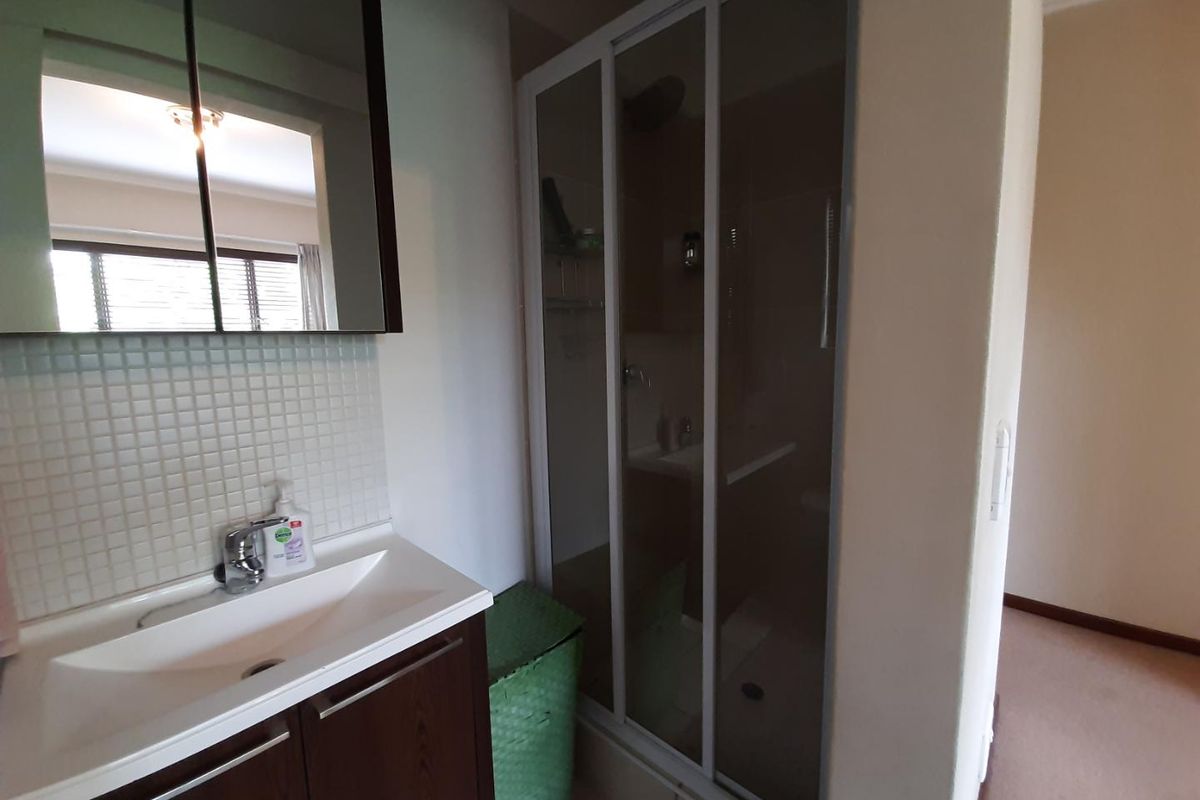A functional bathroom featuring a vanity with basin, a mirrored medicine cabinet, and a glass-enclosed shower with mosaic tile detailing.