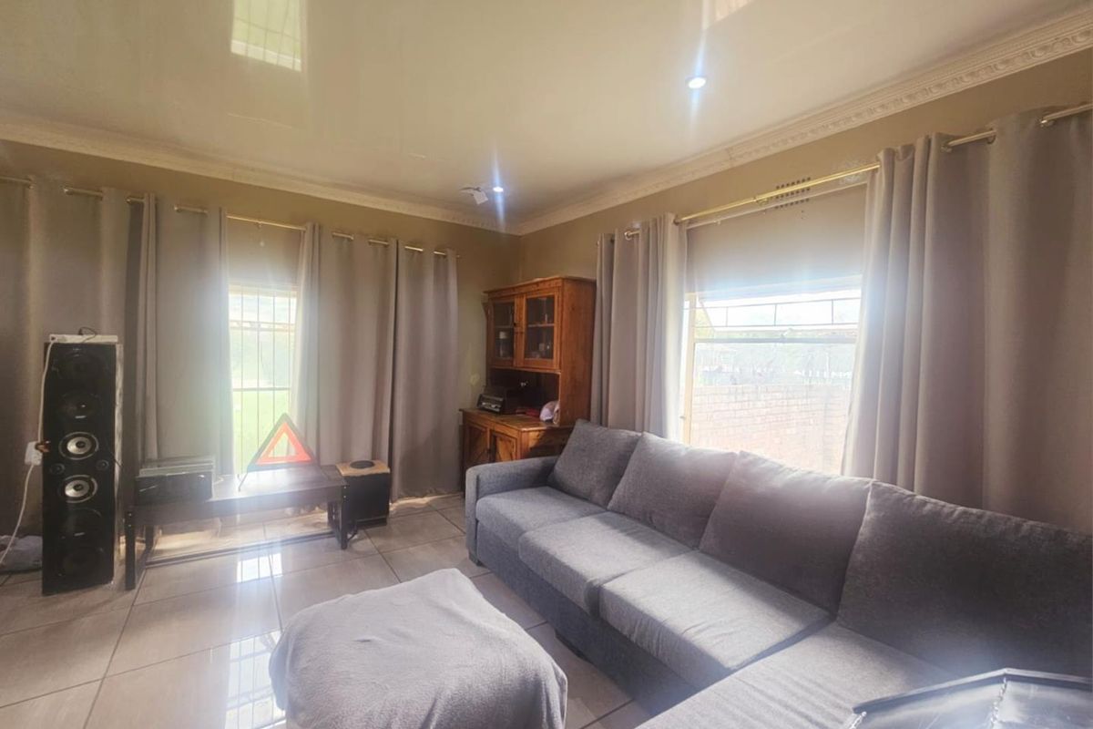 A living room featuring large windows with curtain tracks, tiled flooring, and decorative ceiling cornicing.