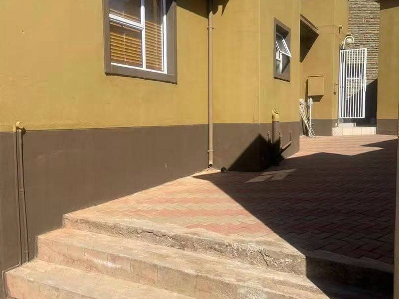 Rear exterior view showing paved walkway, concrete steps, and building facade with satellite dish and security gate.