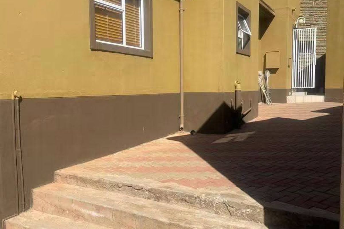 Rear exterior view showing paved walkway, concrete steps, and building facade with satellite dish and security gate.